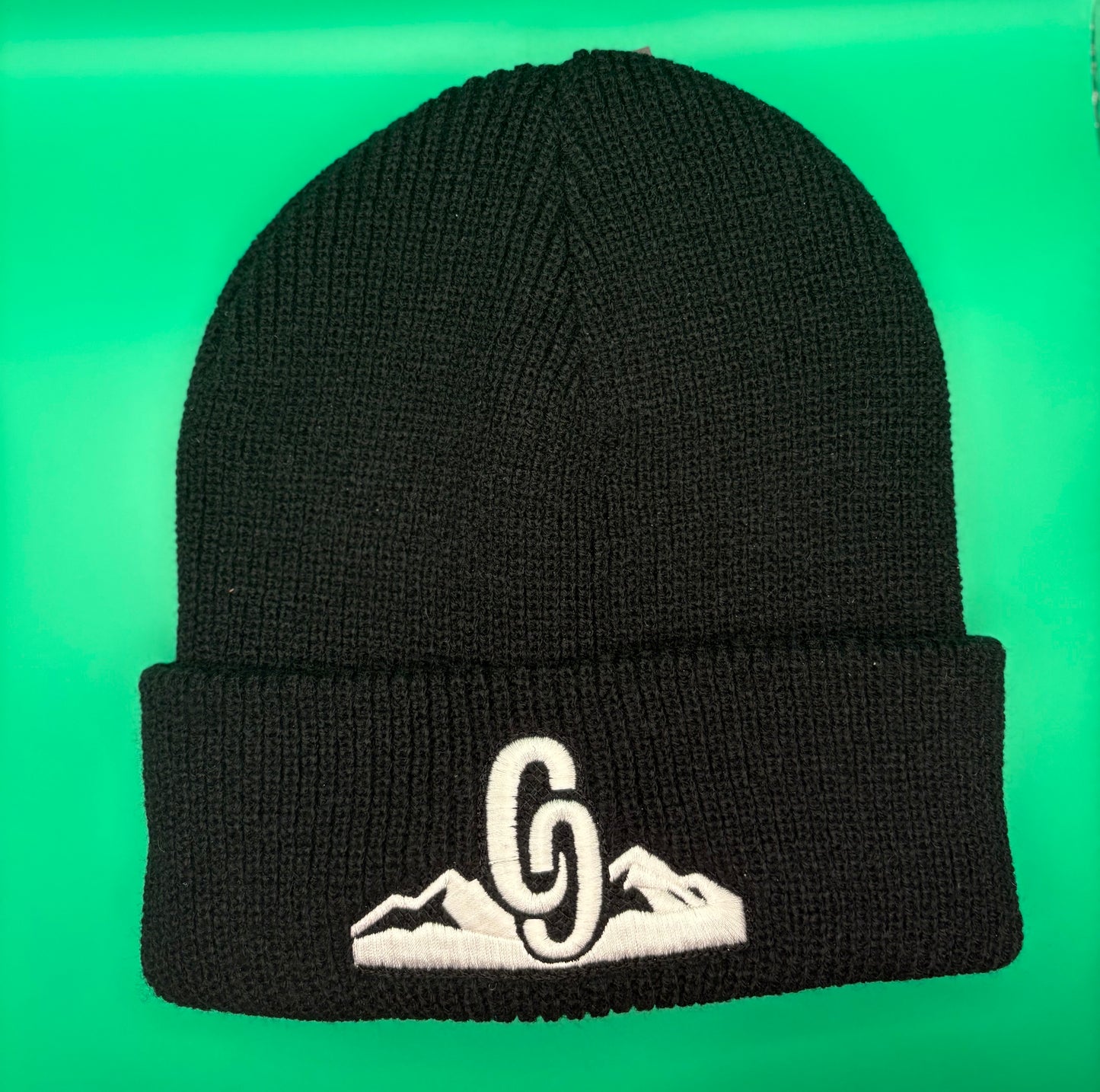 Black beanie with white embroidered design on a green background front view