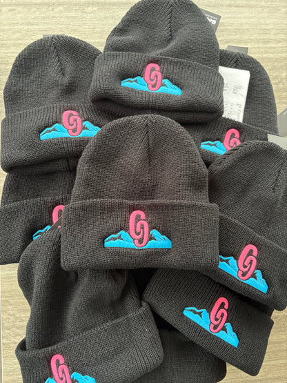 Stack of Blackbeanie hats with colorful logos on a light brown surface country beanie
