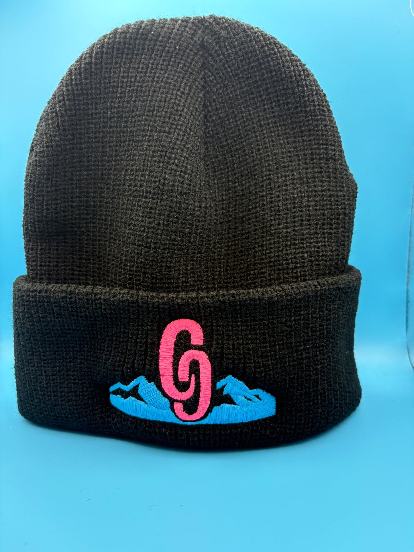 Black beanie with pink and blue logo on a blue background country
