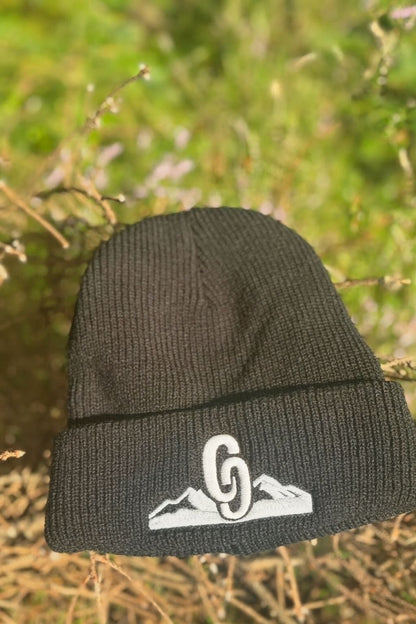 Black beanie with a white logo embroidered on a natural background front view