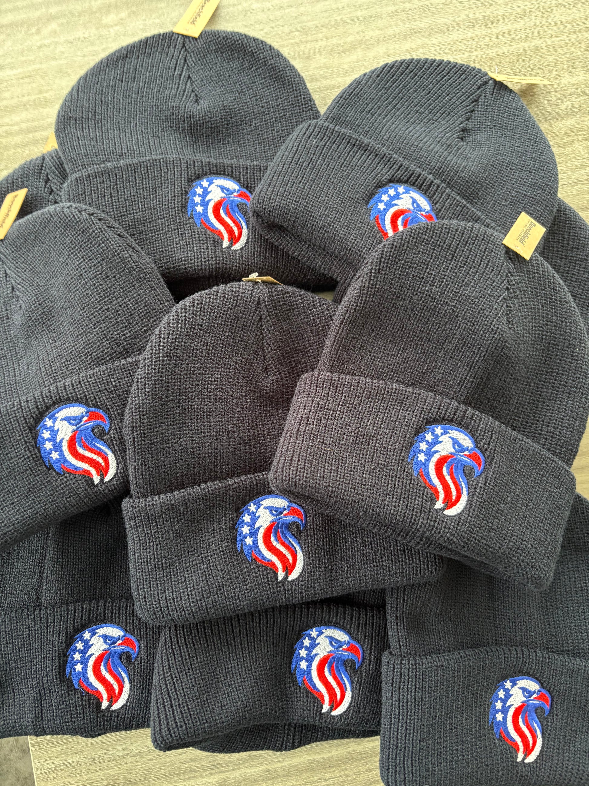 Stack of Navy knit hats with a logo on a light brown surface