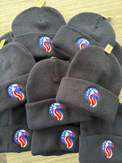 Stack of Navy knit hats with a logo on a light brown surface
