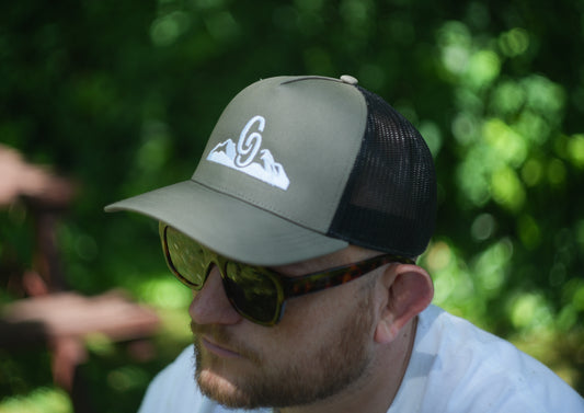 Man wearing a green country cap with a logo and sunglasses, outdoors. side view snapback